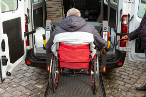 Elderly man in wheel chair being lifted into a minibus